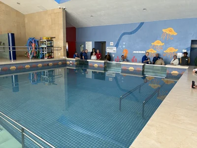 Indoor pool; group in blue shirts along edge near counter; yellow jellyfish mural on blue wall.