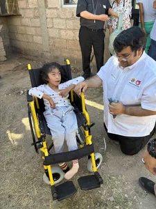 Young girl in a bright yellow wheelchair, assisted by a man in a white shirt; spectators nearby.