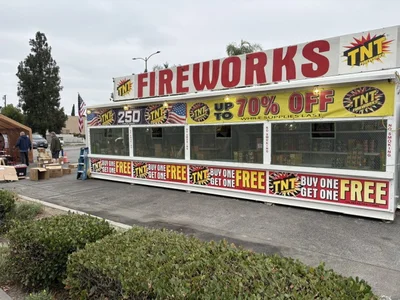 Large TNT Fireworks stand with '70% OFF' and 'BUY ONE GET ONE FREE' signs and green bushes.