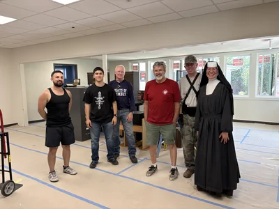 Six people, including a nun in a black habit, pose in a large room with blue tape on the floor.