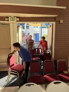 Young men moving and arranging red chairs through an open exit doorway.