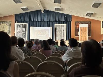 Audience watching a presentation about the Shroud of Turin on a large screen in a hall.