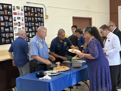 People in blue shirts and a woman in purple serve food at a blue buffet table.